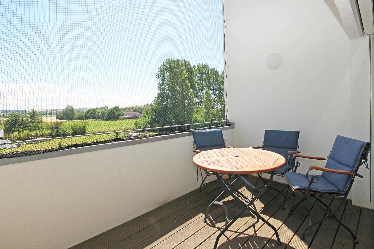 Terrasse mit Tisch und drei Stühlen, Blick auf grüne Landschaft.
