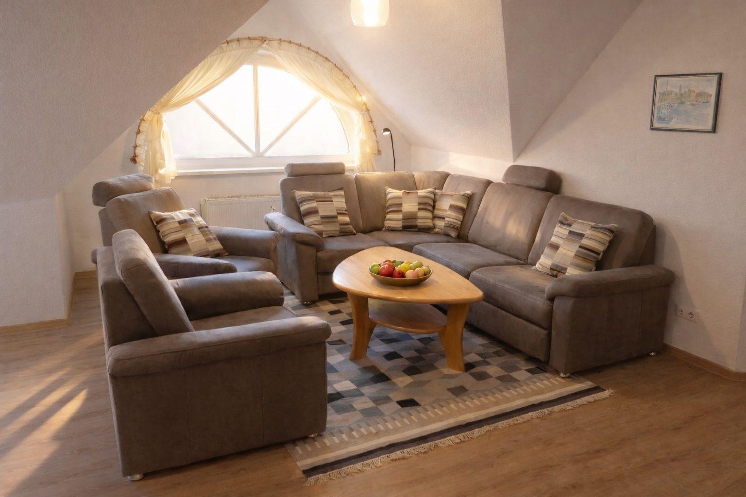 Wohnzimmer mit Sofa, Sesseln und runden Tisch unter Dachschrägen mit Fenster.