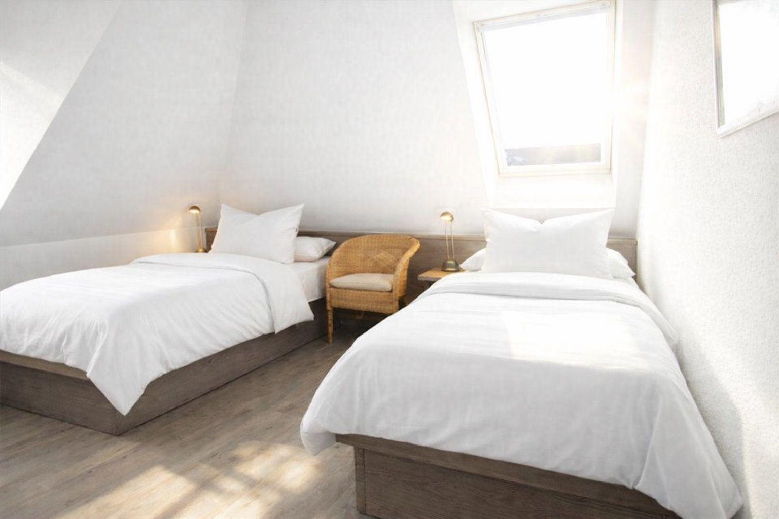 Zwei Betten mit weißen Laken, Stuhl und Fenster in einem Schlafzimmer.