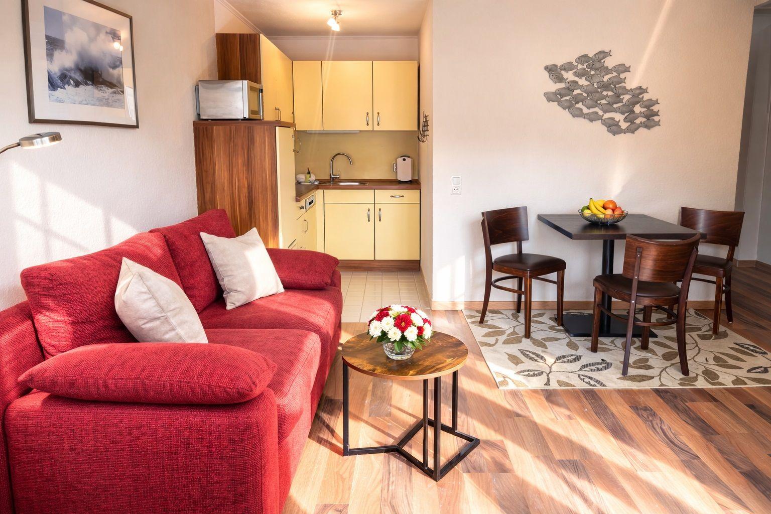 Ein Wohnbereich mit rotem Sofa, Essplatz und Küchenbereich.
