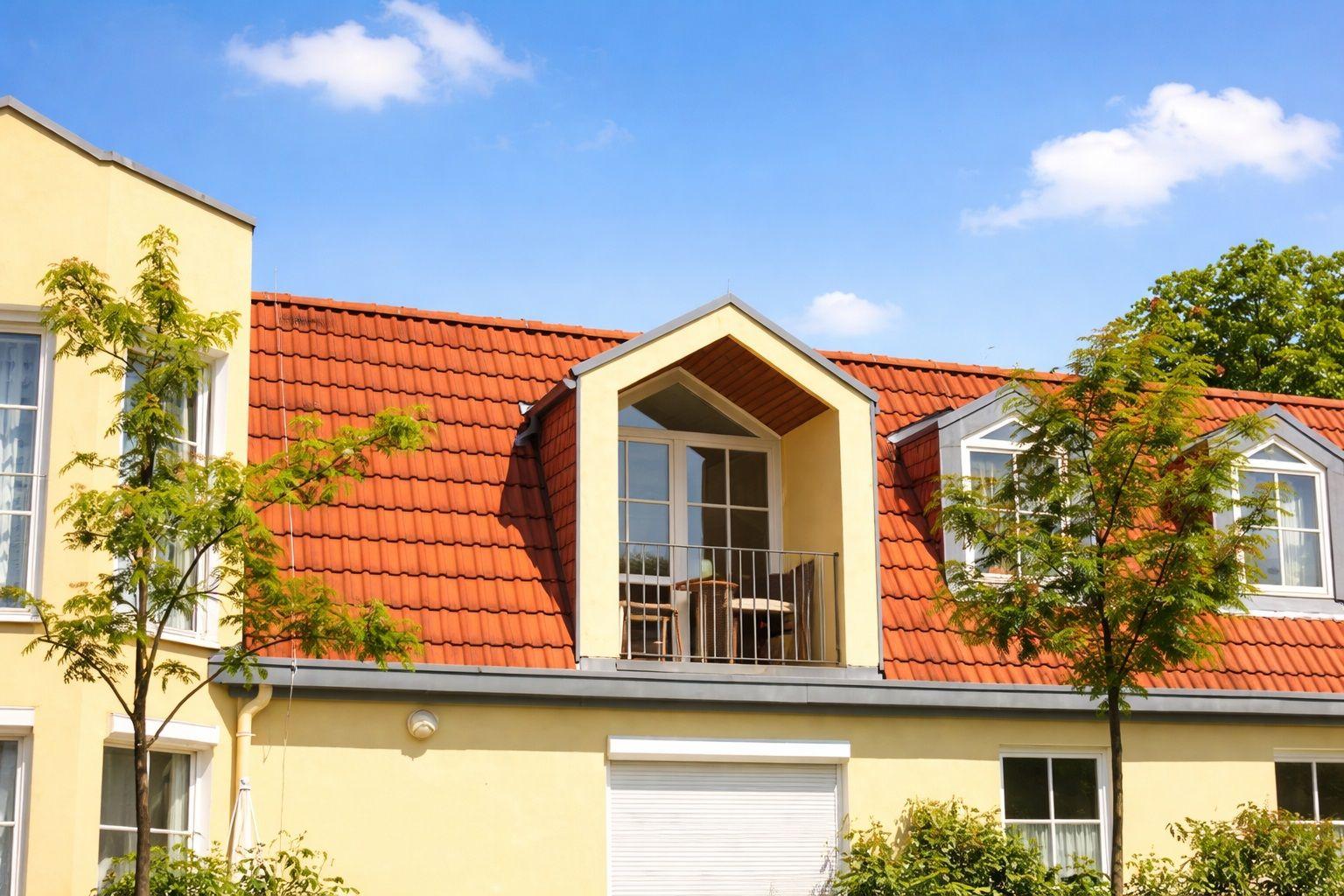 Fassade mit rotem Dach und Dachterrasse mit Tischen und Stühlen.