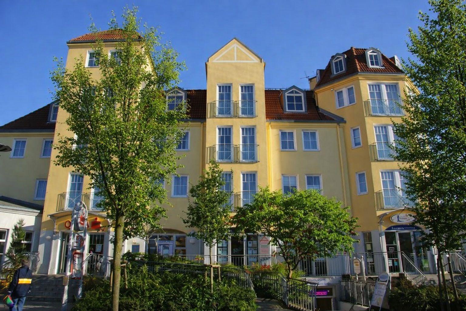 Gelbes Mehrfamilienhaus mit Balkonen und rotem Dach unter blauem Himmel.