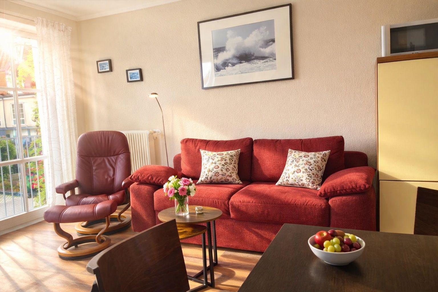 Ein Wohnzimmer mit rotem Sofa, einem Sessel und einer Glastür zum Balkon.