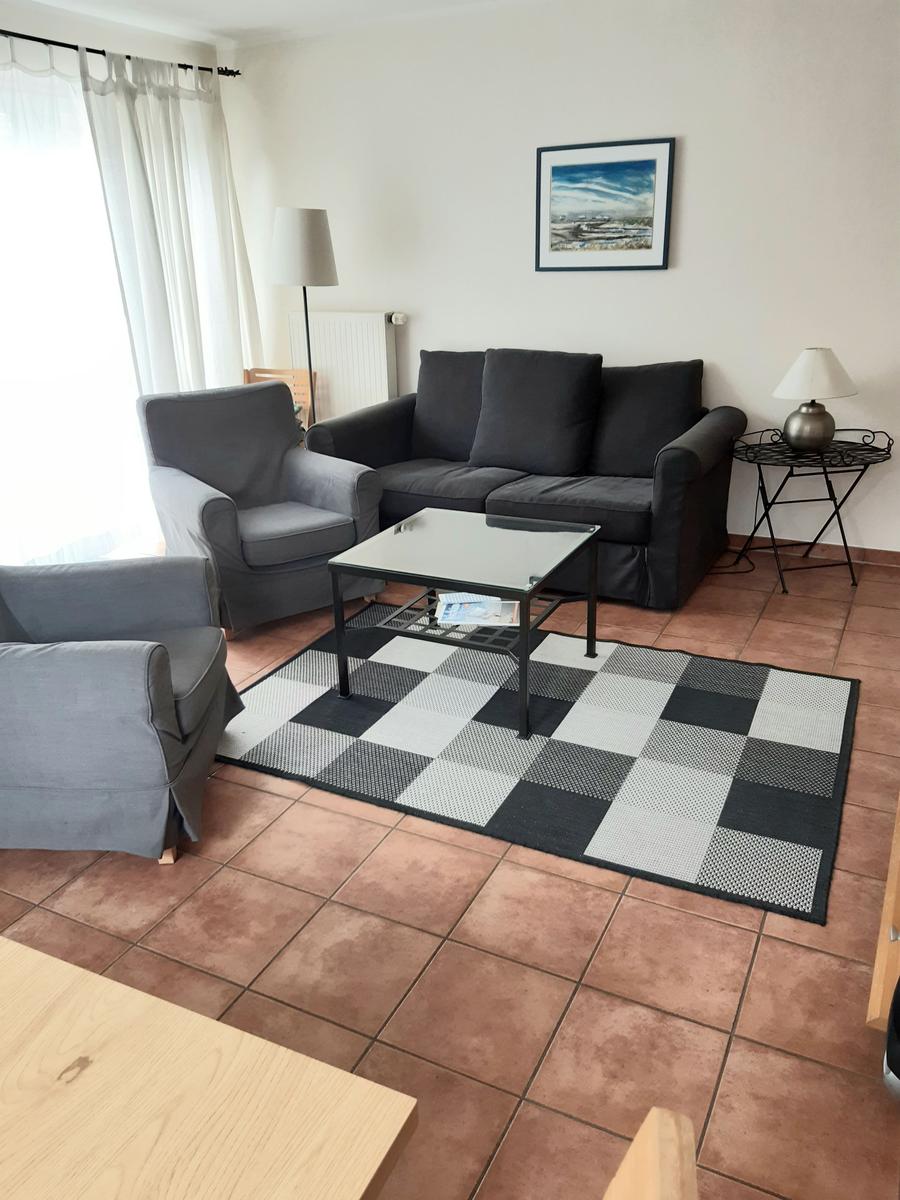 Wohnzimmer mit Sofa, Sessel, Couchtisch und Teppich auf Fliesenboden.