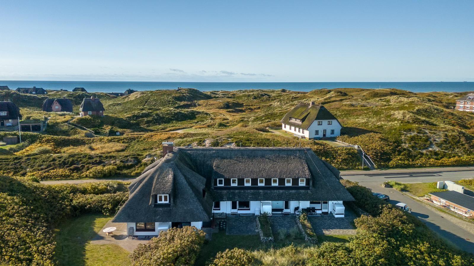 House with thatched roof, surrounded by dunes and sea.