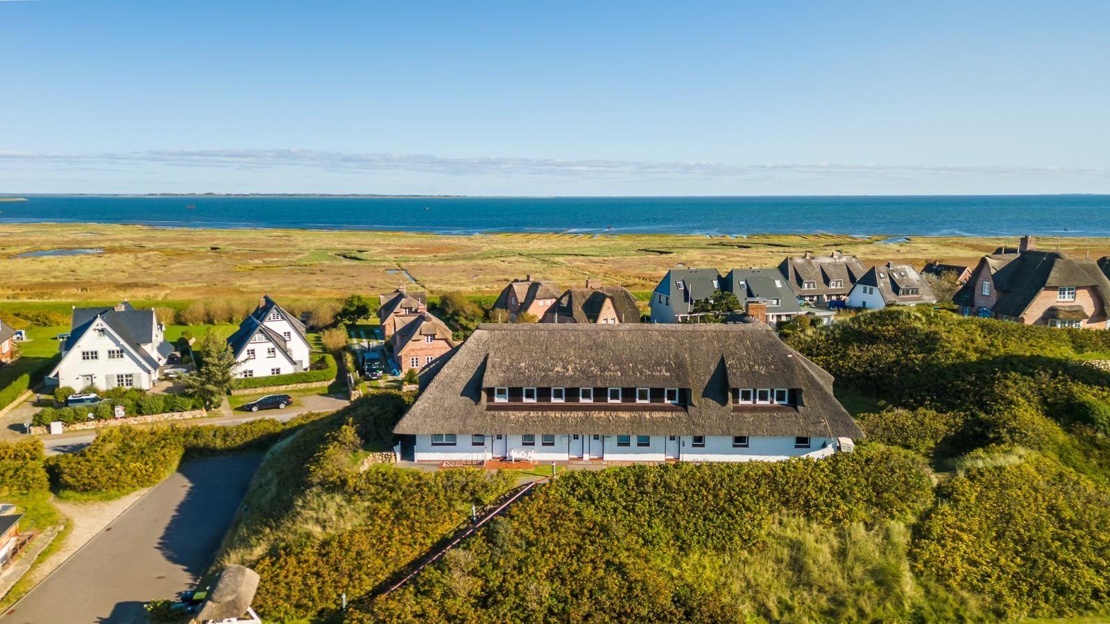 Thatched-roof house surrounded by greenery with a view of the sea.