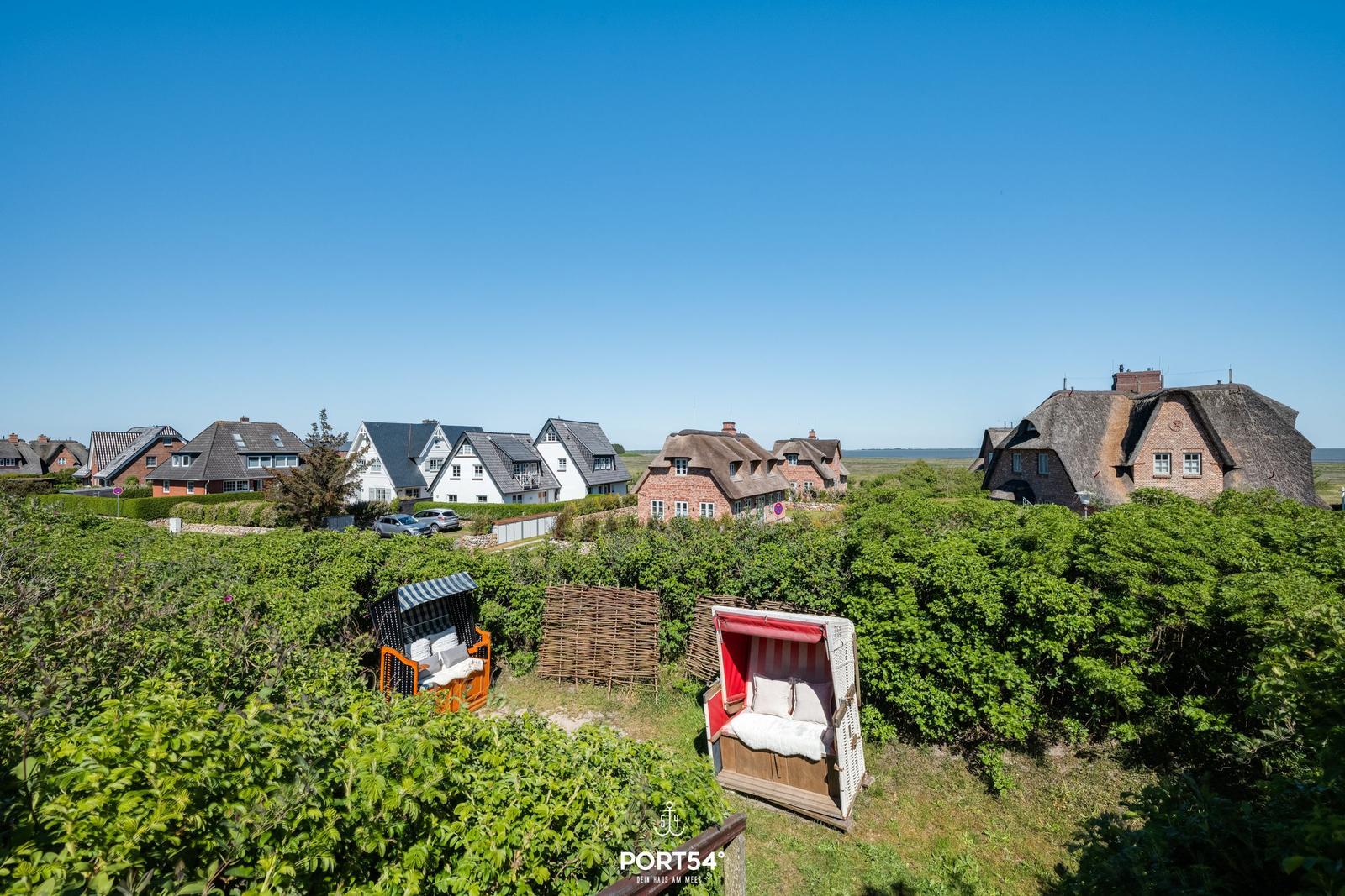 Two beach chairs stand in the green, houses with roofs in the background.