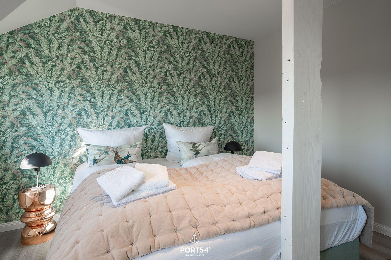 Bedroom with bed, pillows, and floral wallpaper on the wall.