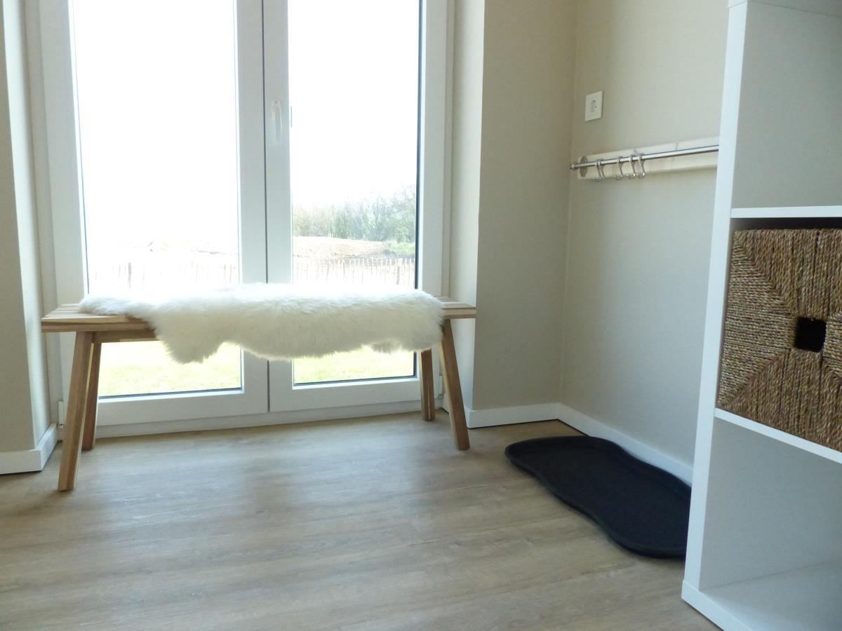 Blick auf eine Bank mit Felldecke vor einer Glastür. Neben einem Kleiderständer und einem Korb.
