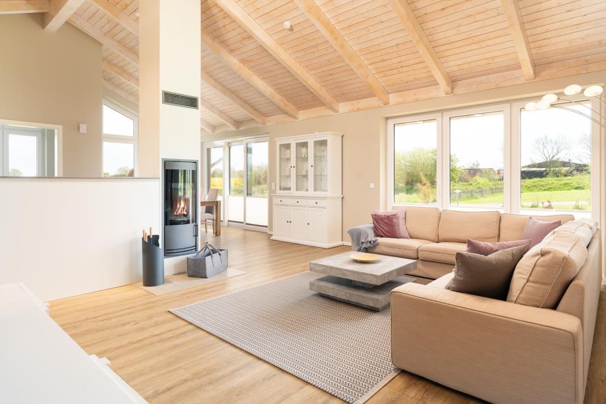 Wohnzimmer mit Holzdecke, Kamin und großem Sofa. Fenster bieten Blick auf die Landschaft.