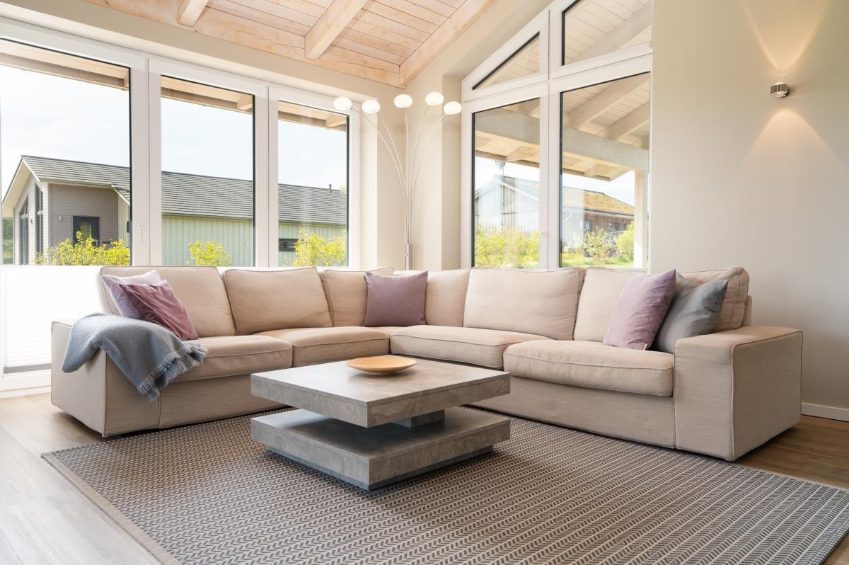 Wohnzimmer mit Ecksofa, Couchtisch und großen Fenstern.