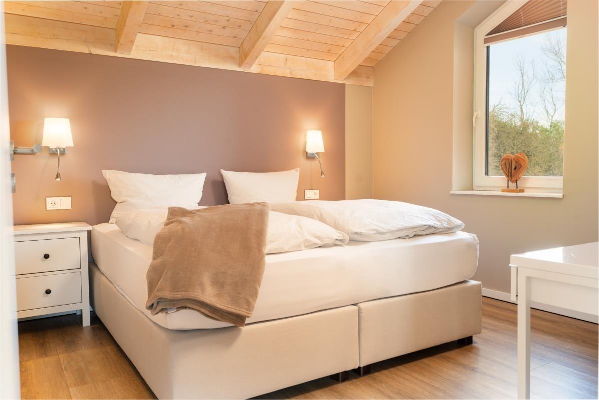 Schlafzimmer mit Doppelbett, Holzdecke und Fenster. Neben dem Bett steht ein Nachttisch.
