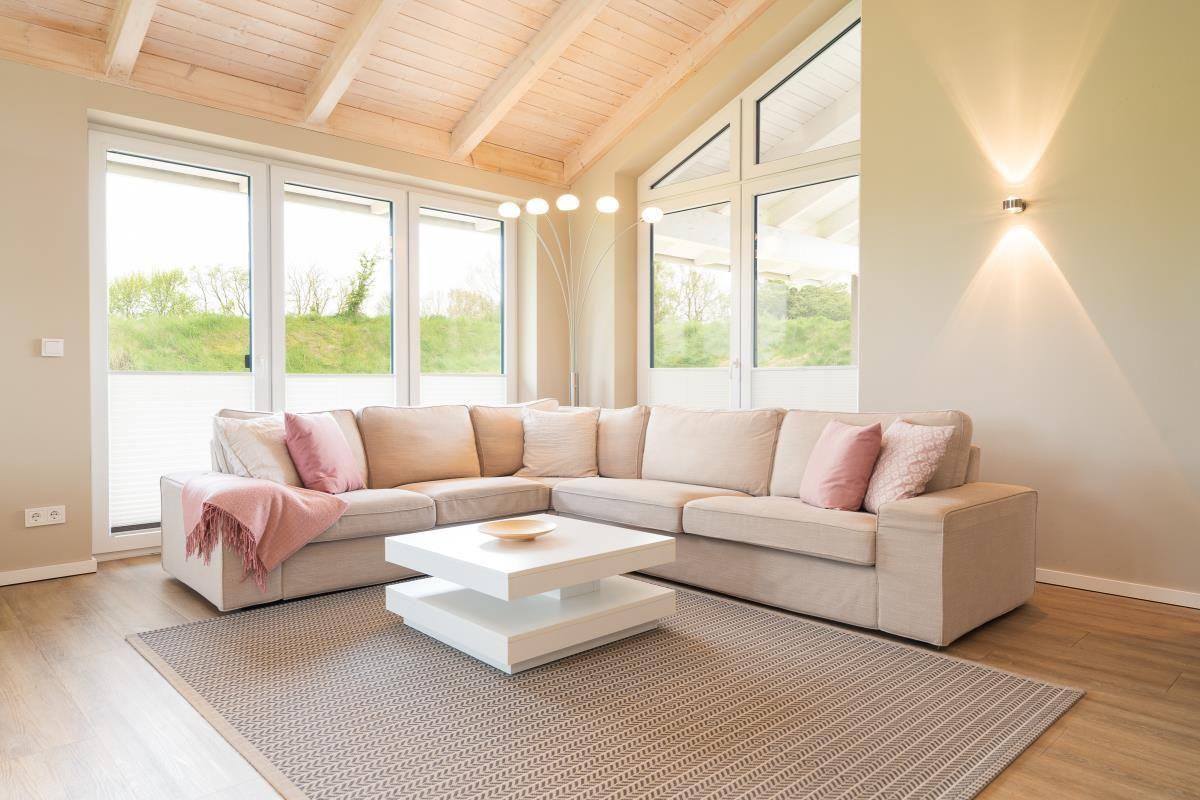 Wohnzimmer mit großem Sofa, weißen Fenstern und Holzdecke.
