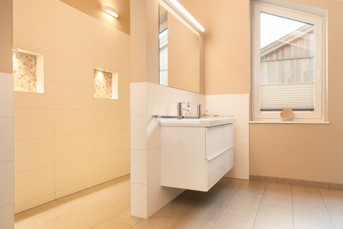 Badezimmer mit Waschbecken, Spiegel und Fenster. Fliesenwand mit eingebauter Mosaiknische.