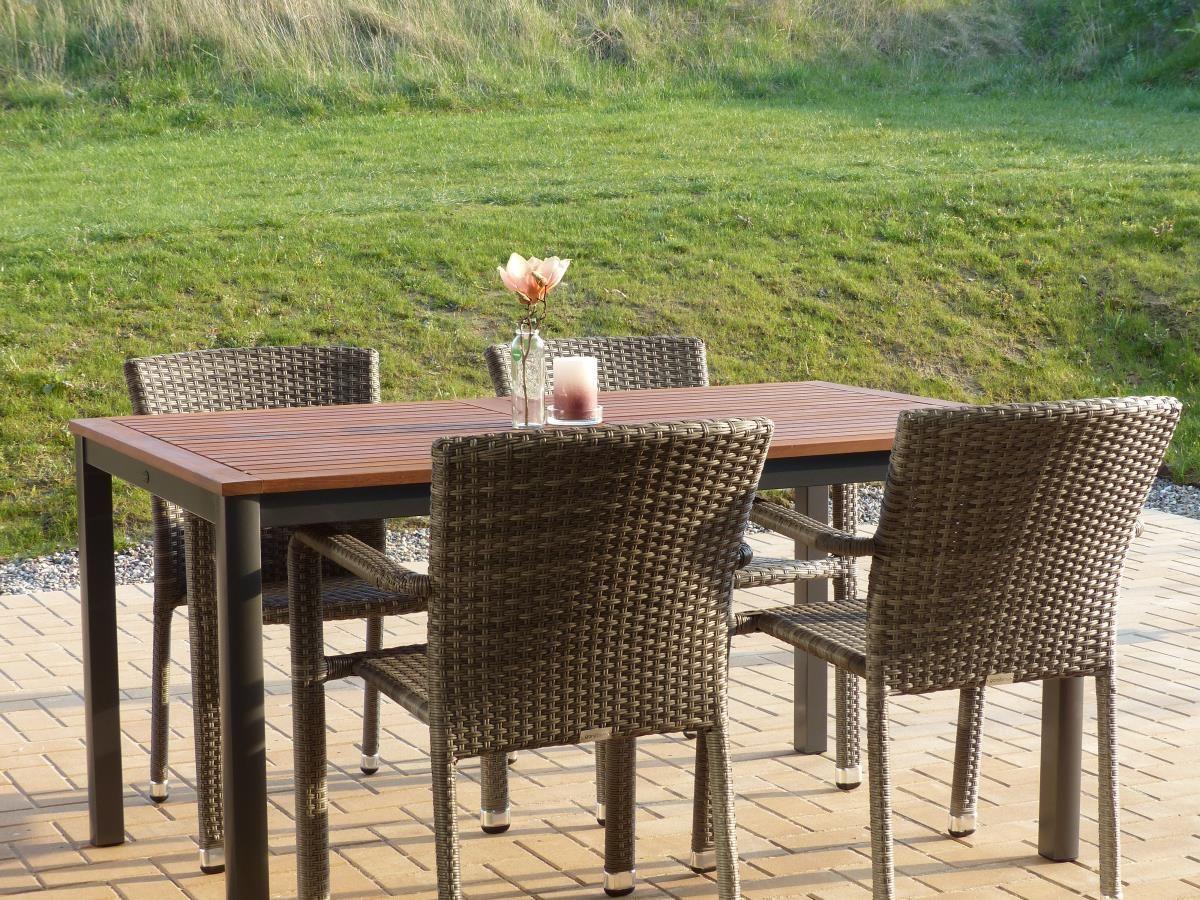 Holztisch mit vier Stühlen auf Terrasse. Hintergrund: grüner Rasenhang.