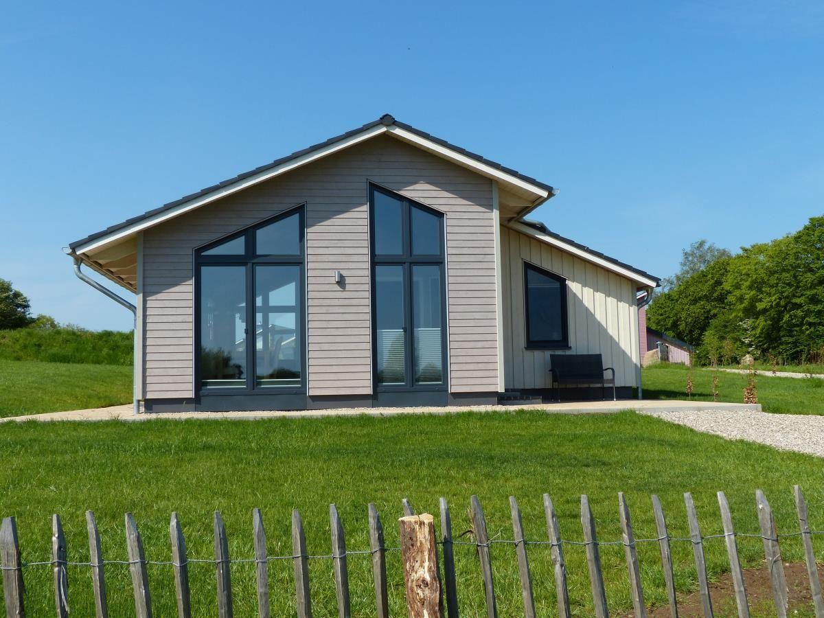 Moderne Holzhütte mit großen Fenstern und Garten. Holzpalisadenzaun im Vordergrund.
