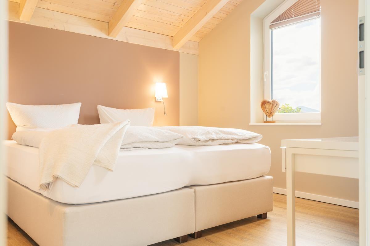 Schlafzimmer mit Doppelbett, Holzdecke und Fenster mit Blick.