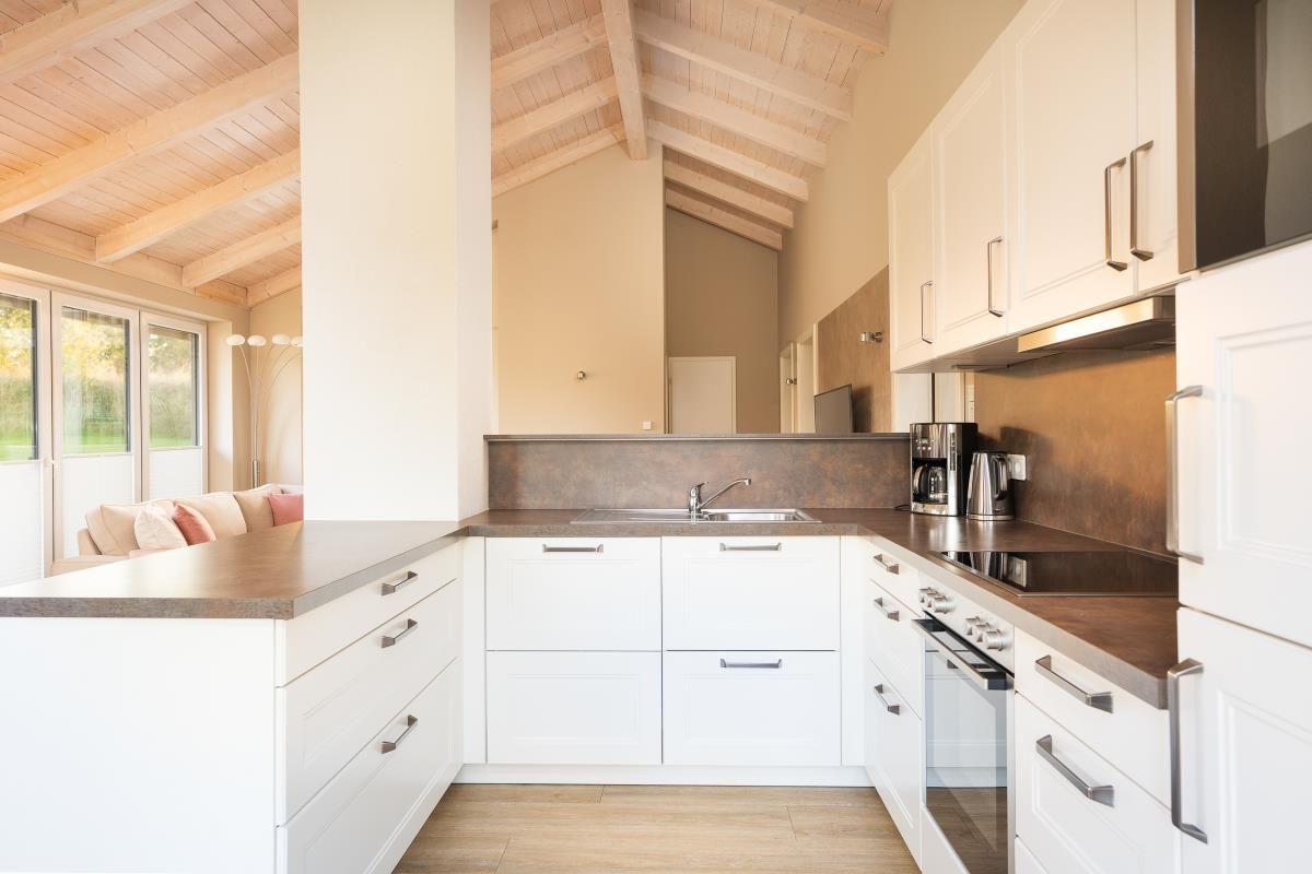 Küche mit weißen Schränken, dunklem Arbeitsplatz und Holzdecke.