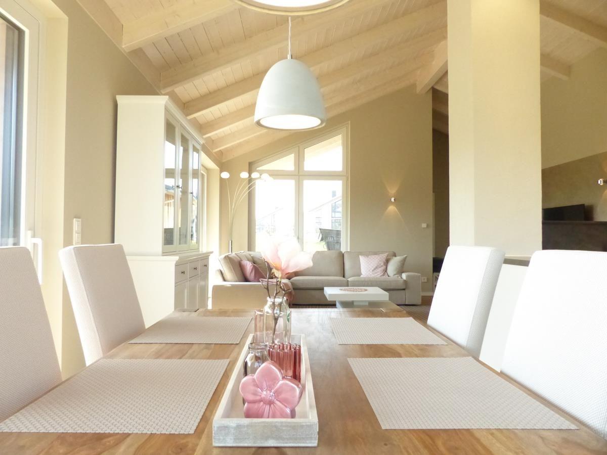 Essbereich mit Holztisch, weißen Stühlen und Blick in Wohnzimmer mit Sofa.