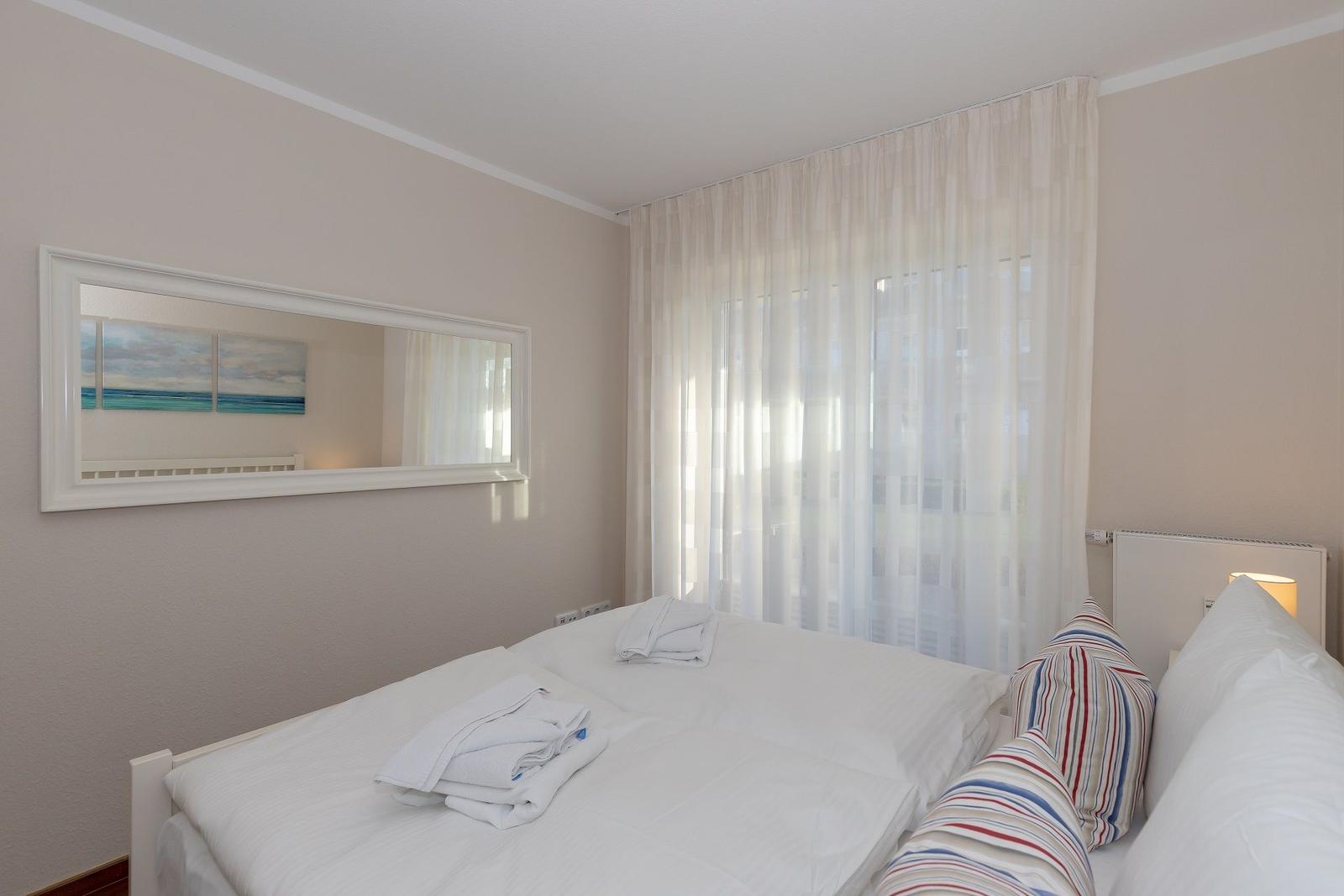 Ein Schlafzimmer mit Bett, Vorhängen und Wandspiegel mit Meeresmotiv.