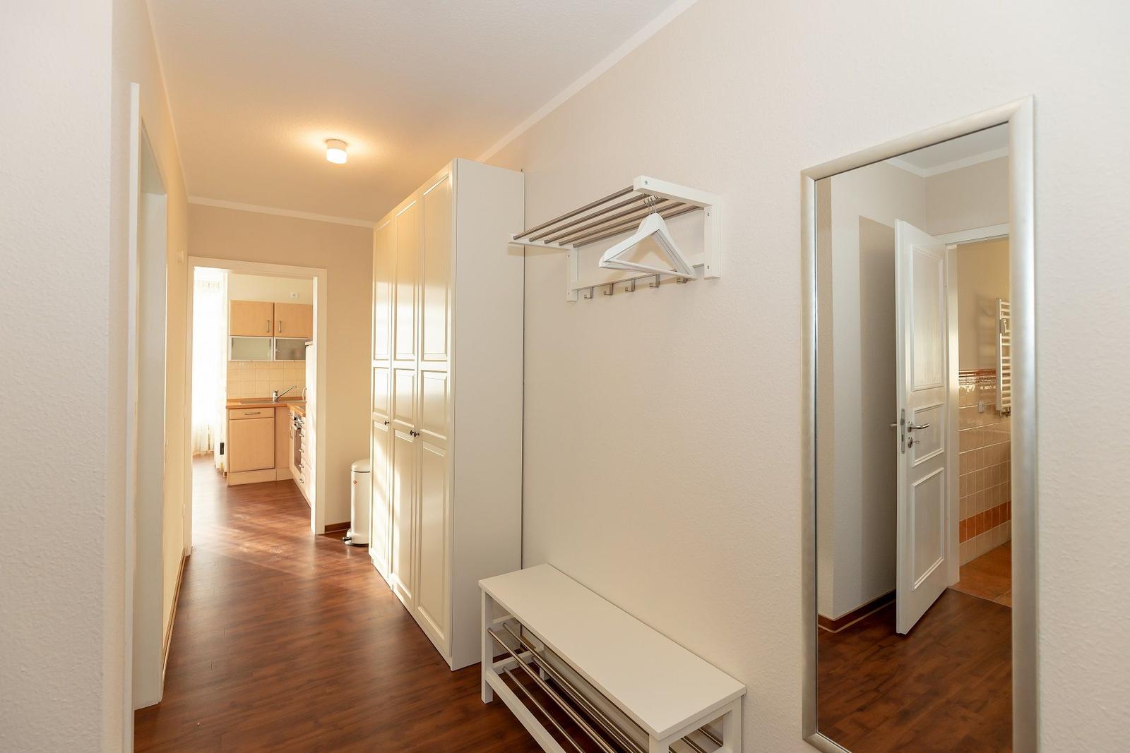 Flur mit Garderobe, Sitzbank und Blick in Küche und Bad.