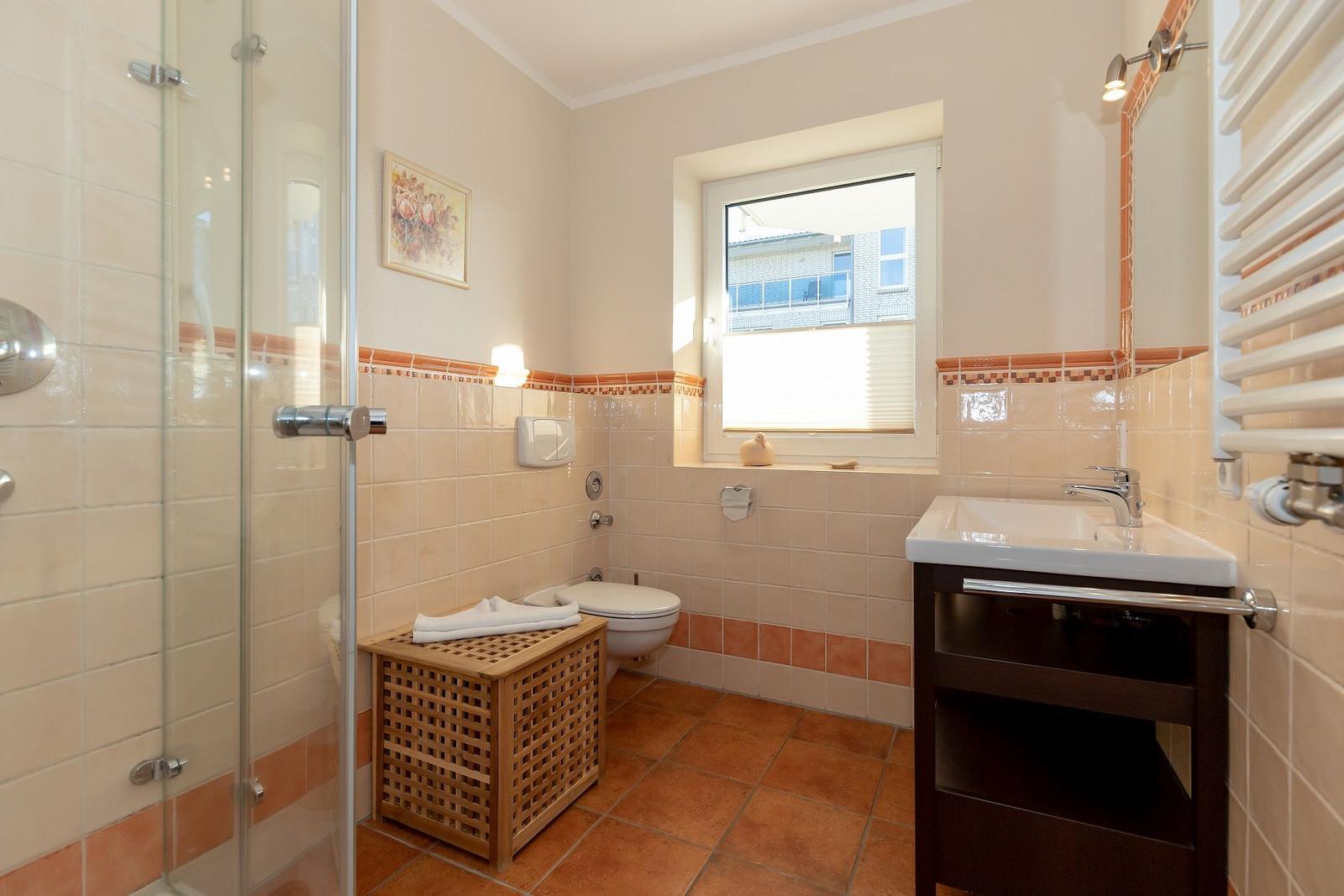 Badezimmer mit Dusche, Toilette, Waschbecken und Fenster.