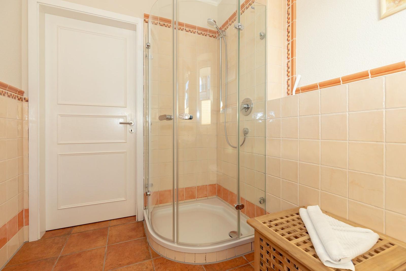 Badezimmer mit Dusche, weiße Tür und Holzbank mit Handtuch.