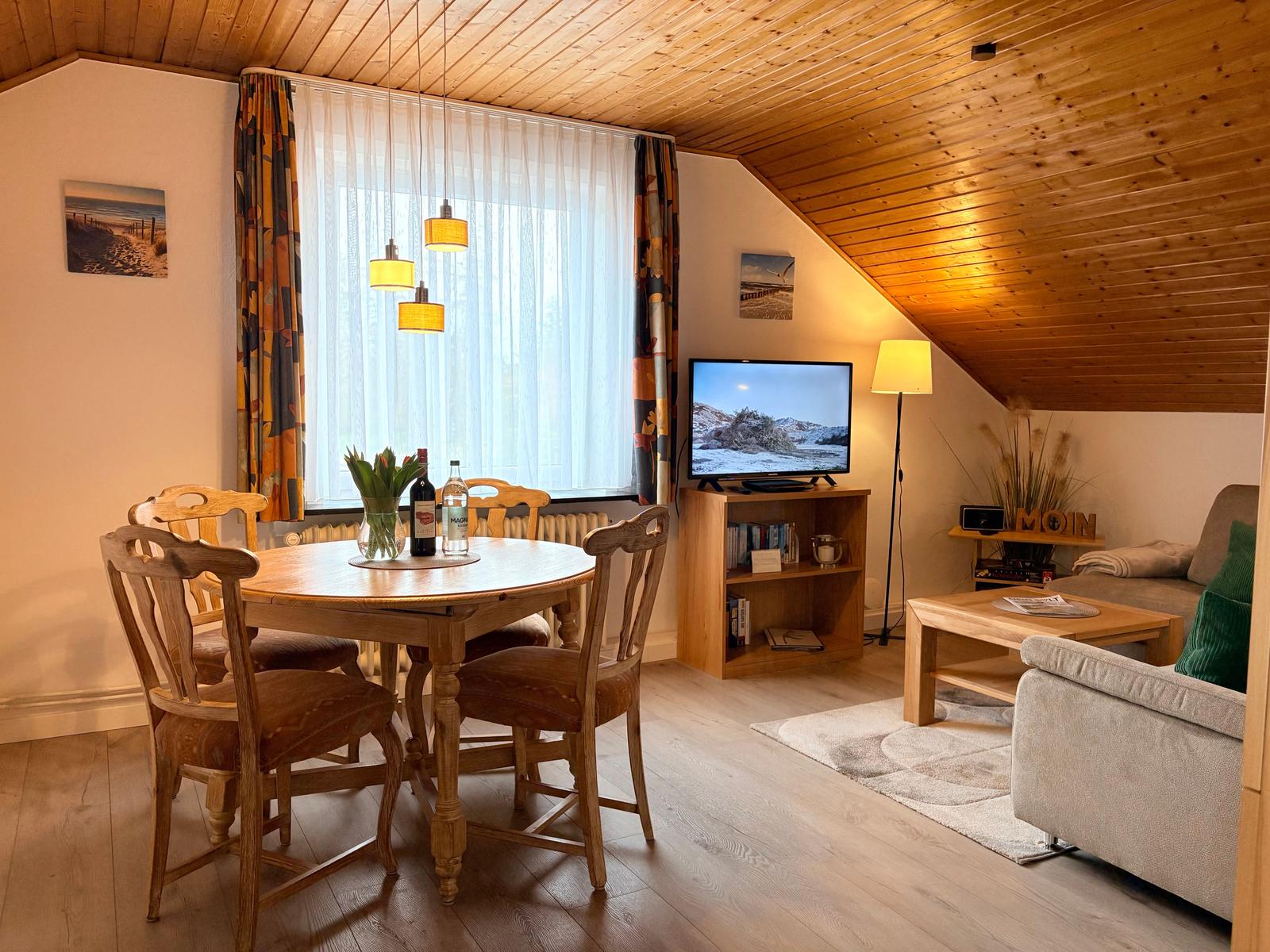 Wohn- und Essbereich mit Holztisch, Sofa und Fernseher unter Holzdach.
