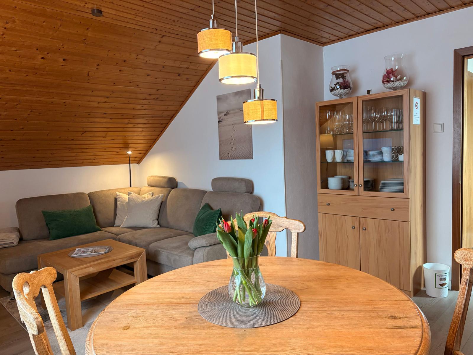 Wohn- und Essbereich mit Holzdecke, Sofa, Esstisch und Sideboard.