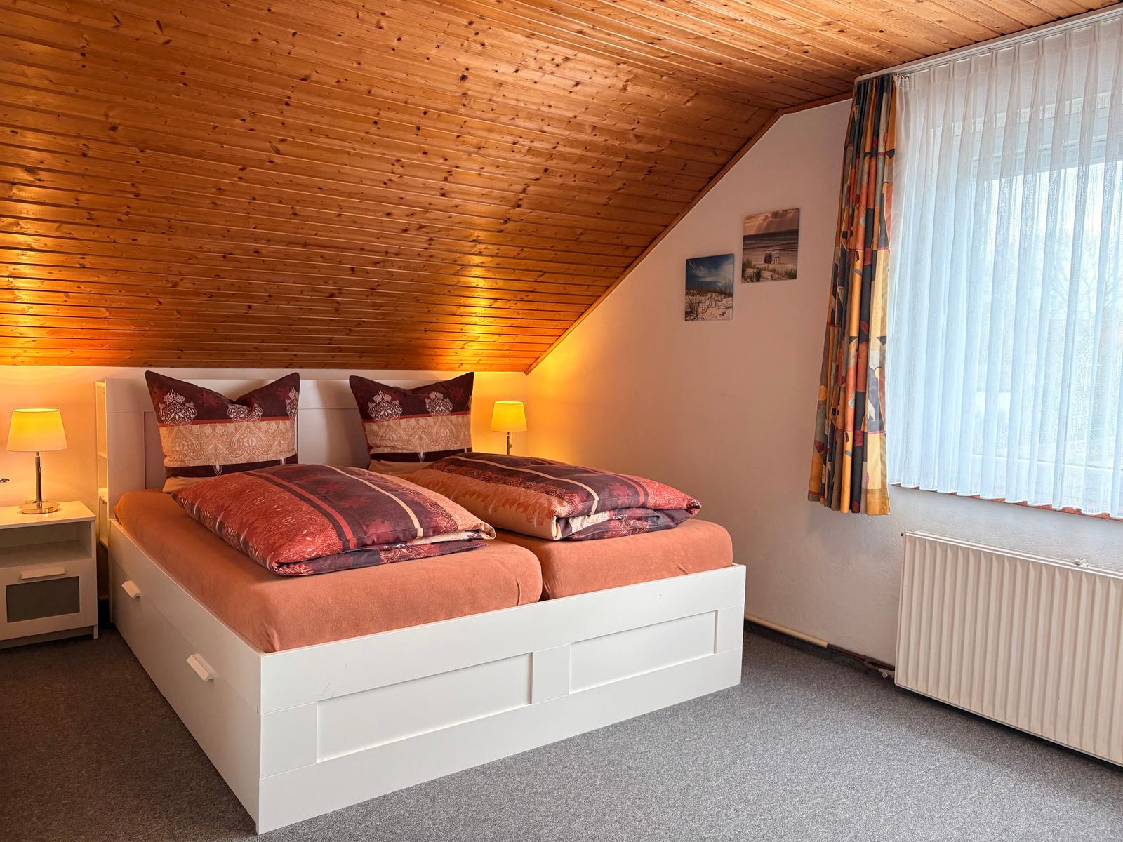 Schlafzimmer mit Doppelbett, Holzdecke und Fenster mit Vorhängen.