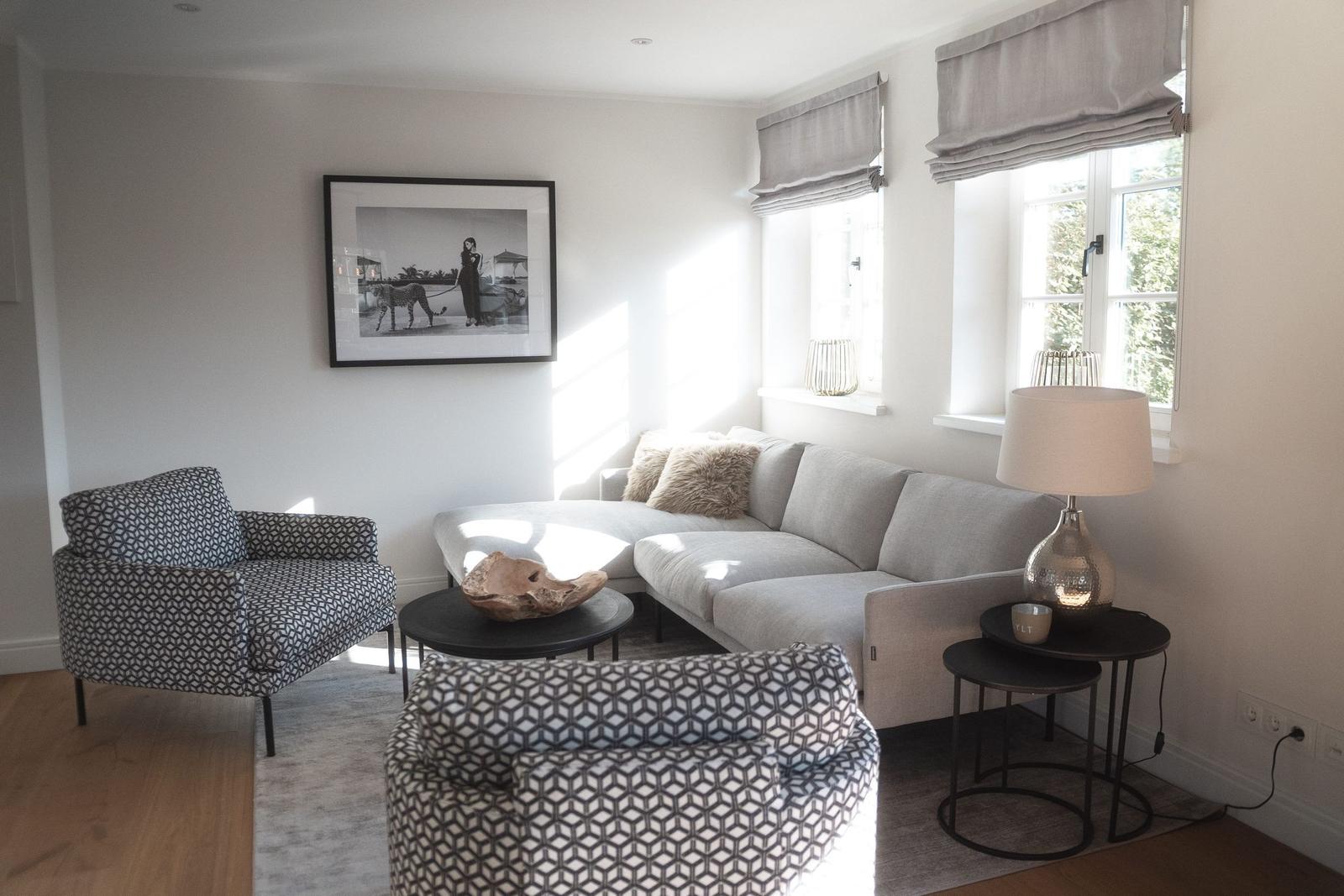 Wohnzimmer mit Sofa, Sessel und Fenstern.