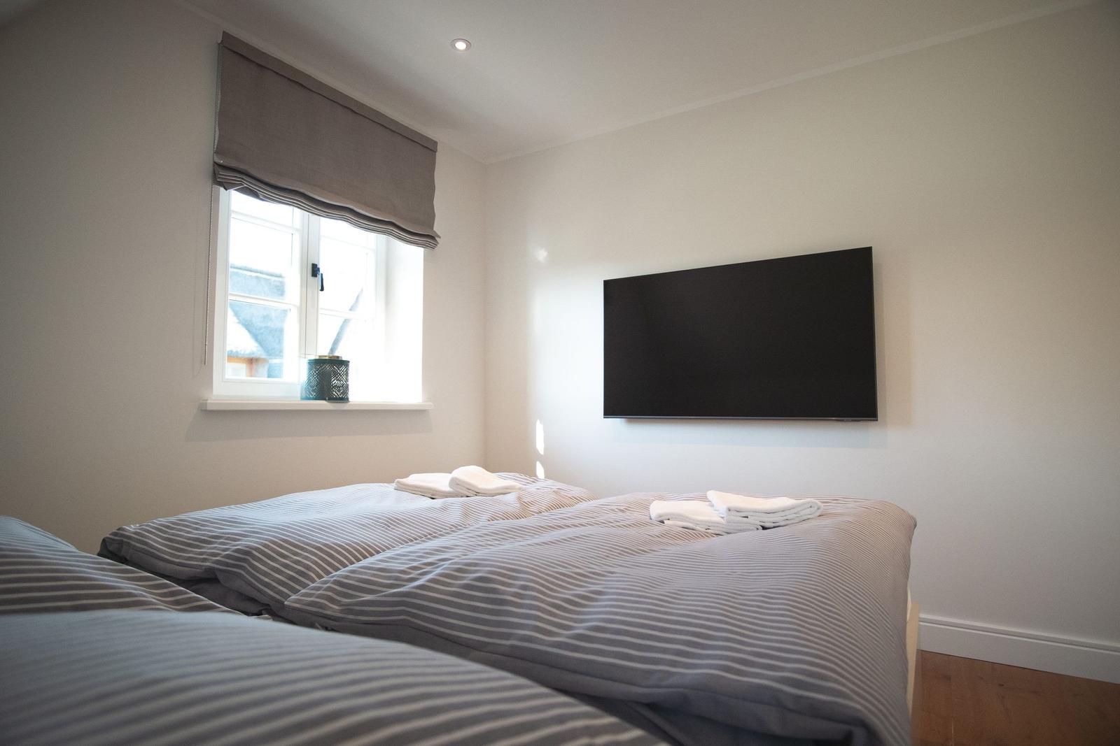 Schlafzimmer mit Bett, Fernseher und Fenster mit Rollladen.