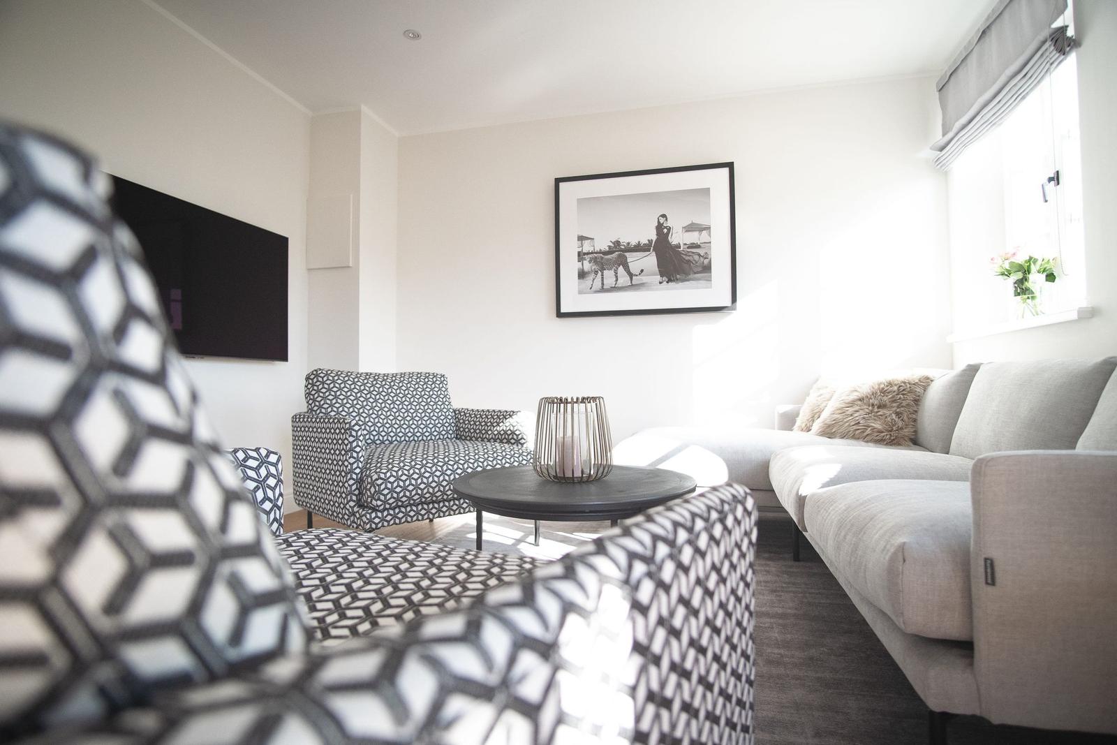 Wohnzimmer mit Sofa, Sessel und Fernseher an der Wand.