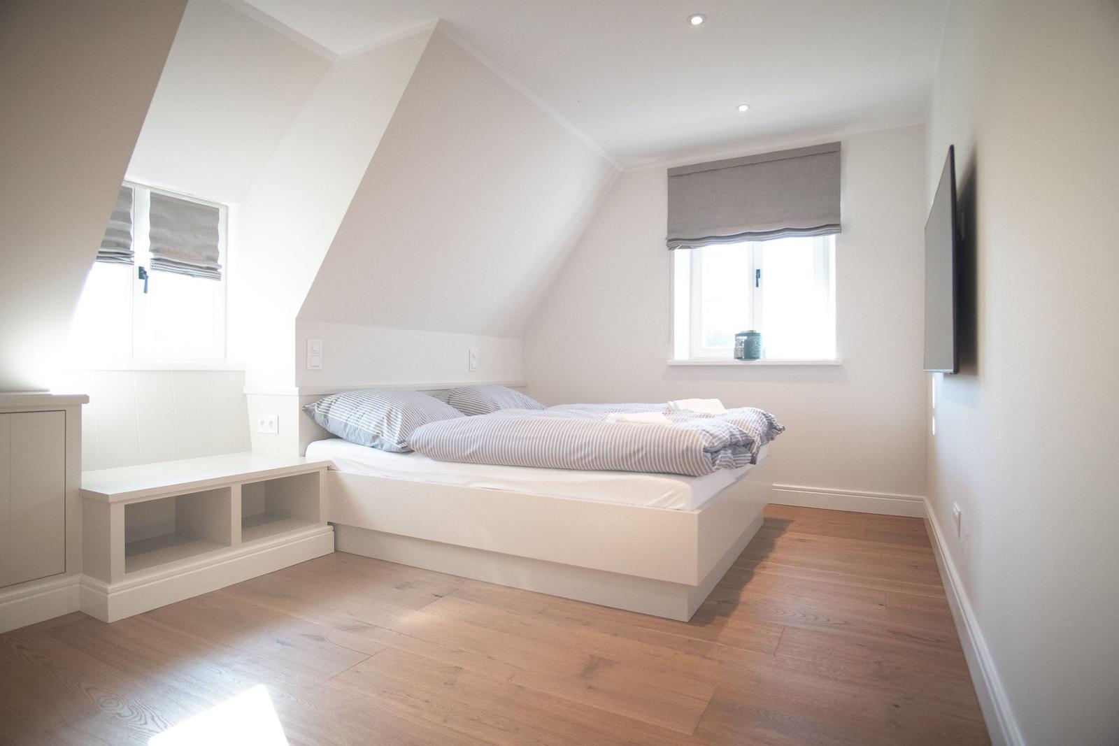 Schlafzimmer mit Doppelbett, Holzboden und Fenstern mit Rollläden.