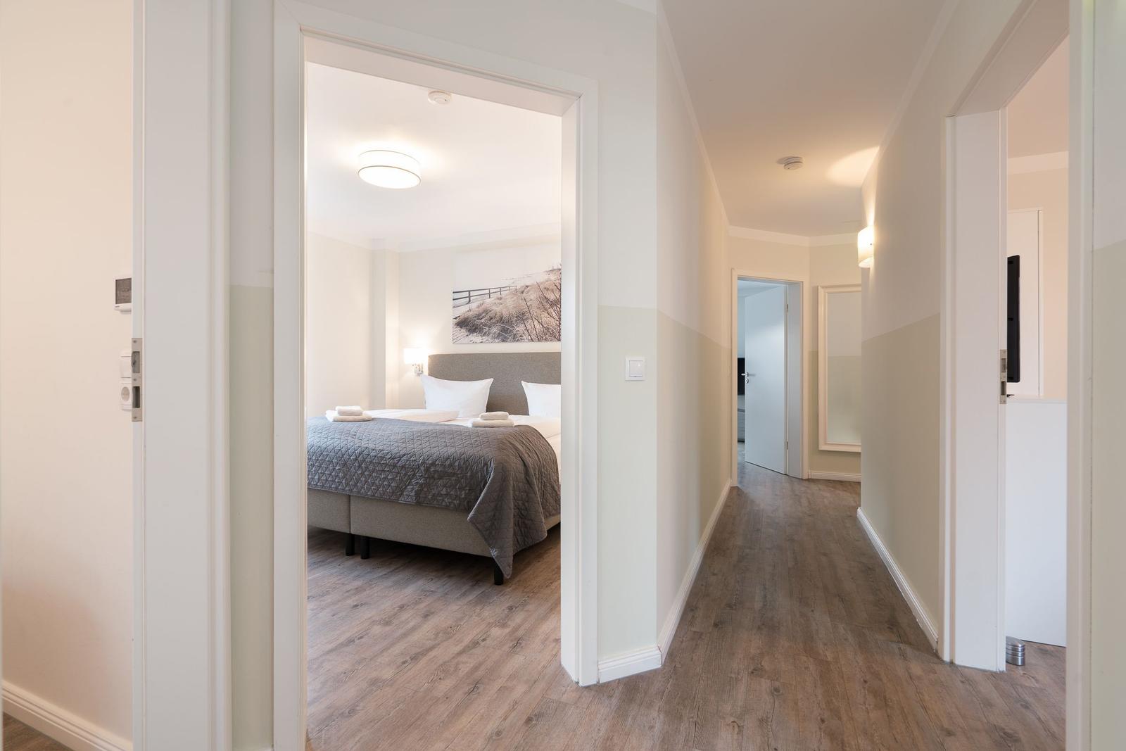 Bedroom with bed and wall art. Hallway with wooden floor and doors.
