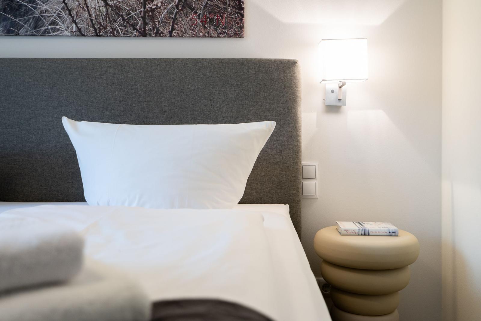 Double bed with white linens, gray headboard, and nightstand with a book.
