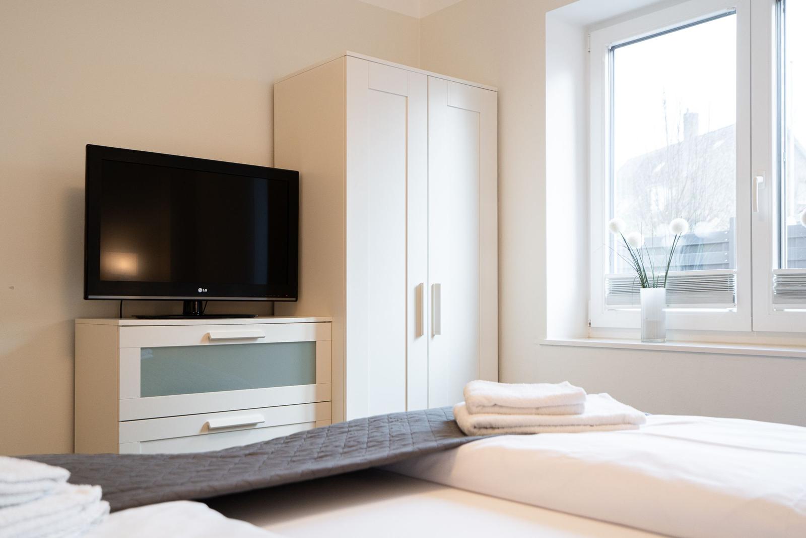Bedroom with bed, wardrobe, and TV. Window with flower vase.