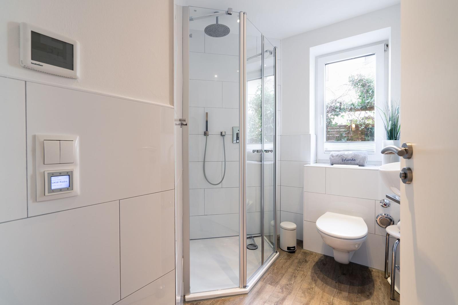 Bathroom with shower, toilet, and sink. Window with view of garden.