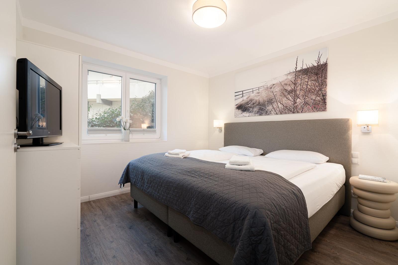 Bedroom with double bed, window, wall art, and TV.