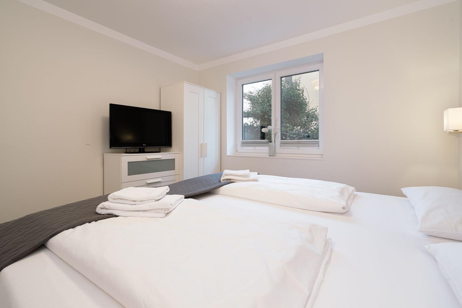Bedroom with bed, TV, and window. Towels are ready.
