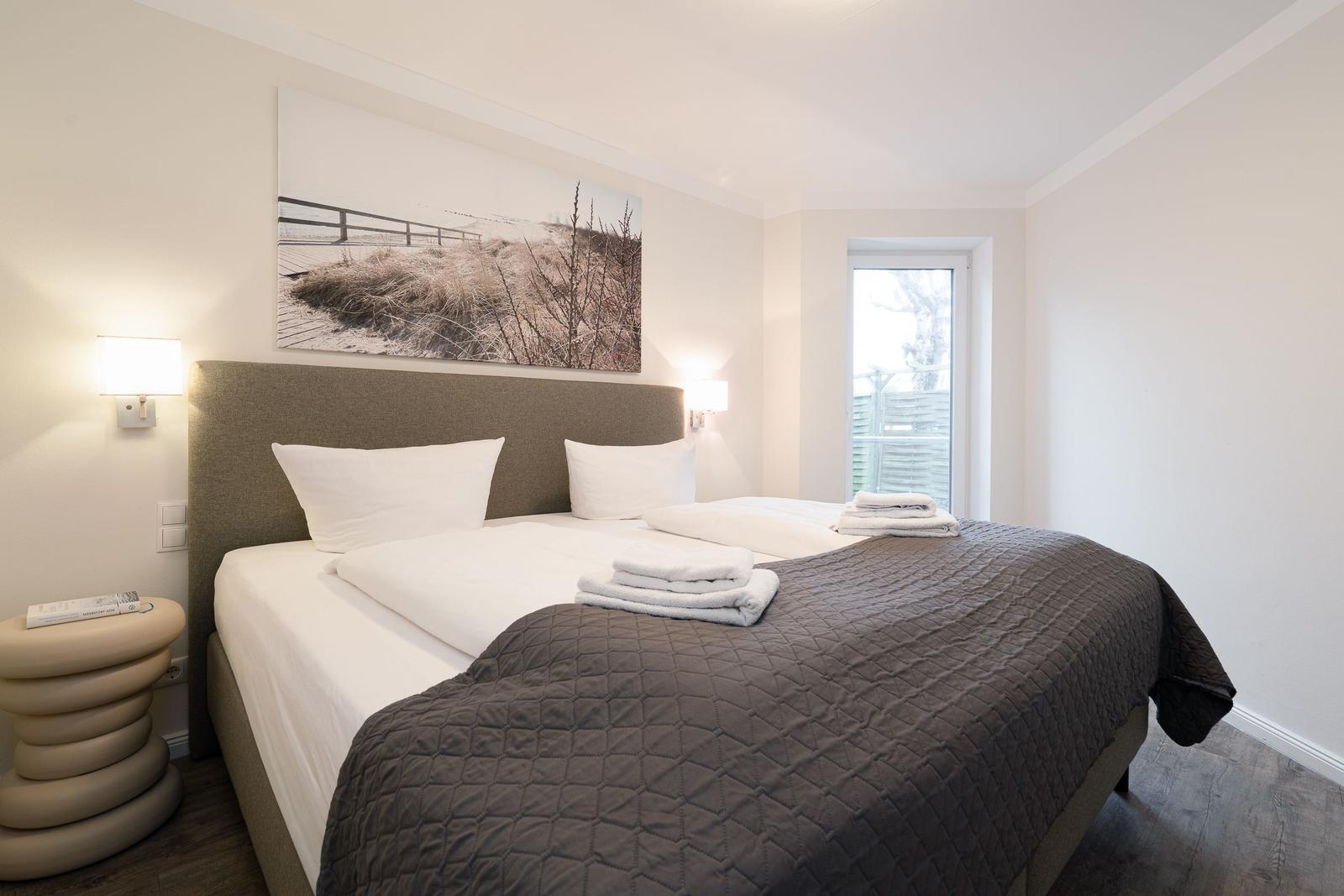Bedroom with double bed, wall art, and window. Bed with cover and towels.