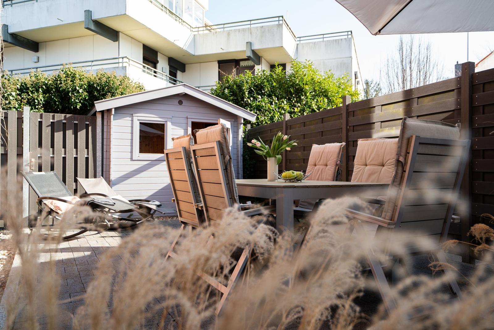 Terrace with seating group, umbrella, and small wooden shed in background.