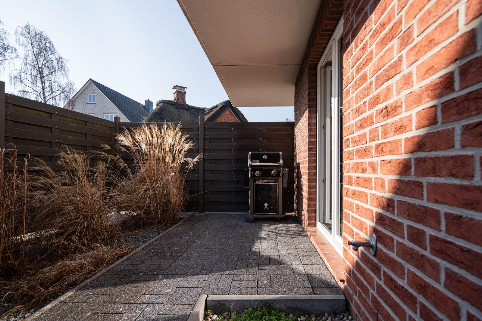 Terrace with grill, red brick house, and wooden fence in background.