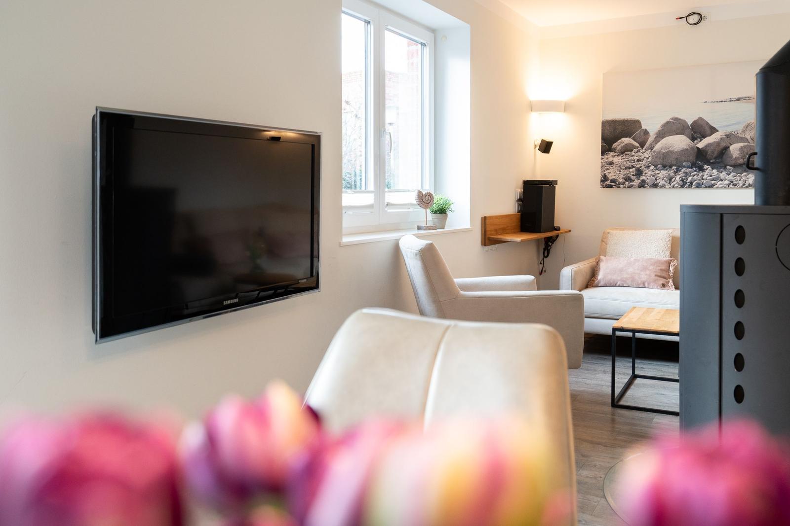 Living room with TV, seating, and window. Flowers in foreground.