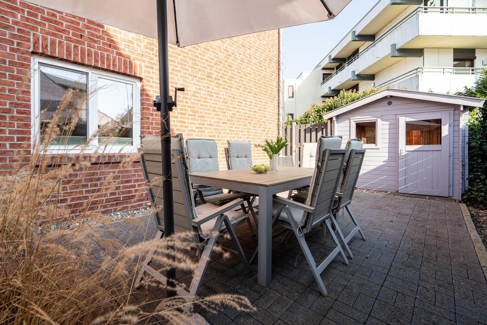 Terrace with table, chairs, and umbrella next to a shed.