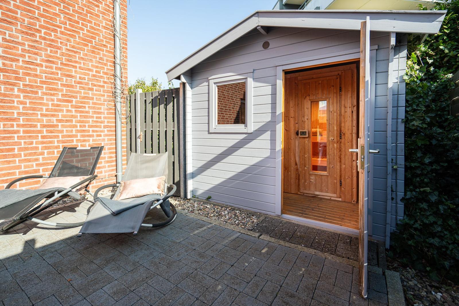 Backyard with sauna, loungers, and paved ground.