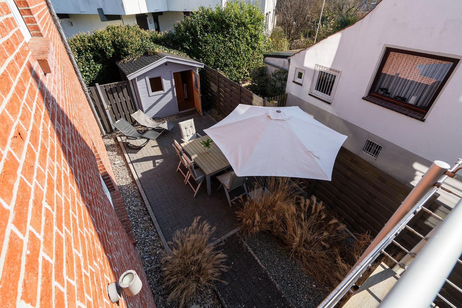 Backyard with table, chairs, and umbrella. Small shed and plants in the garden.