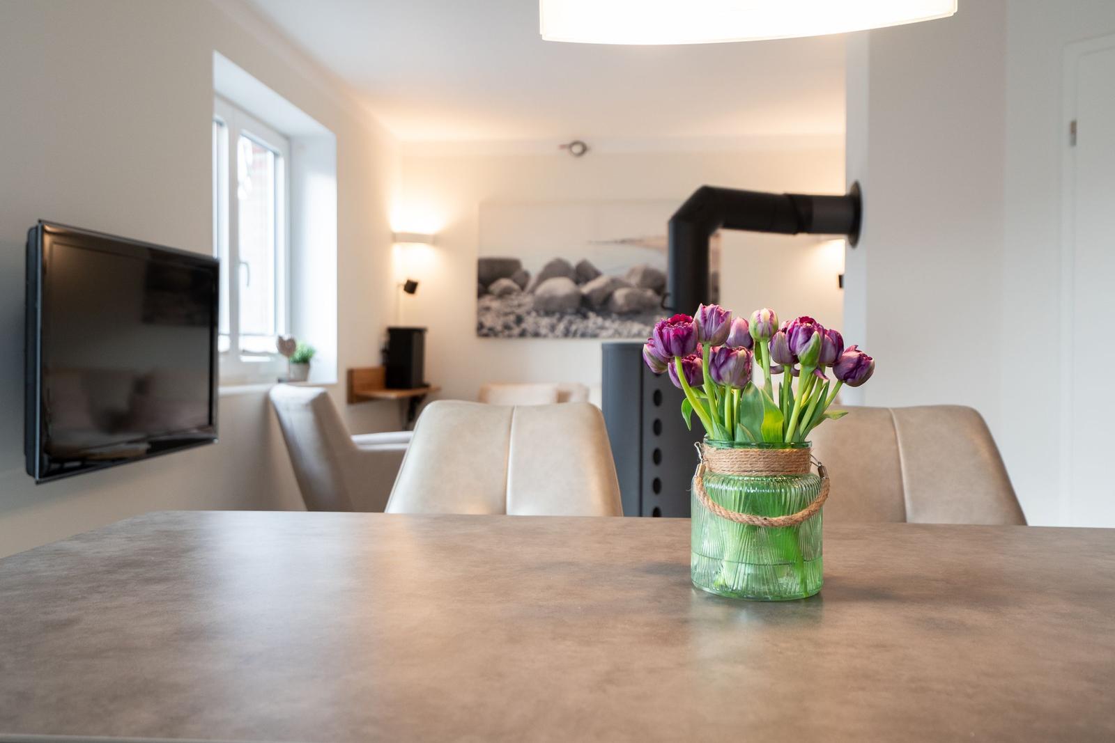 A table with a vase of tulips, with a TV and sofa in the background.