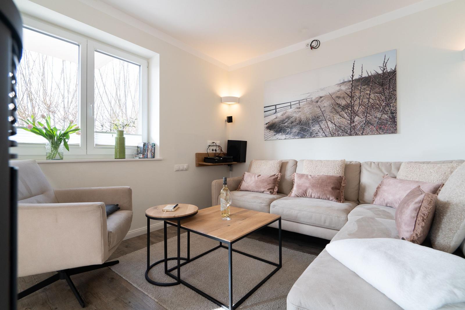 Wohnzimmer mit Sofa, Sessel und Tisch. Fenster, Wandbild und Beleuchtung sichtbar.