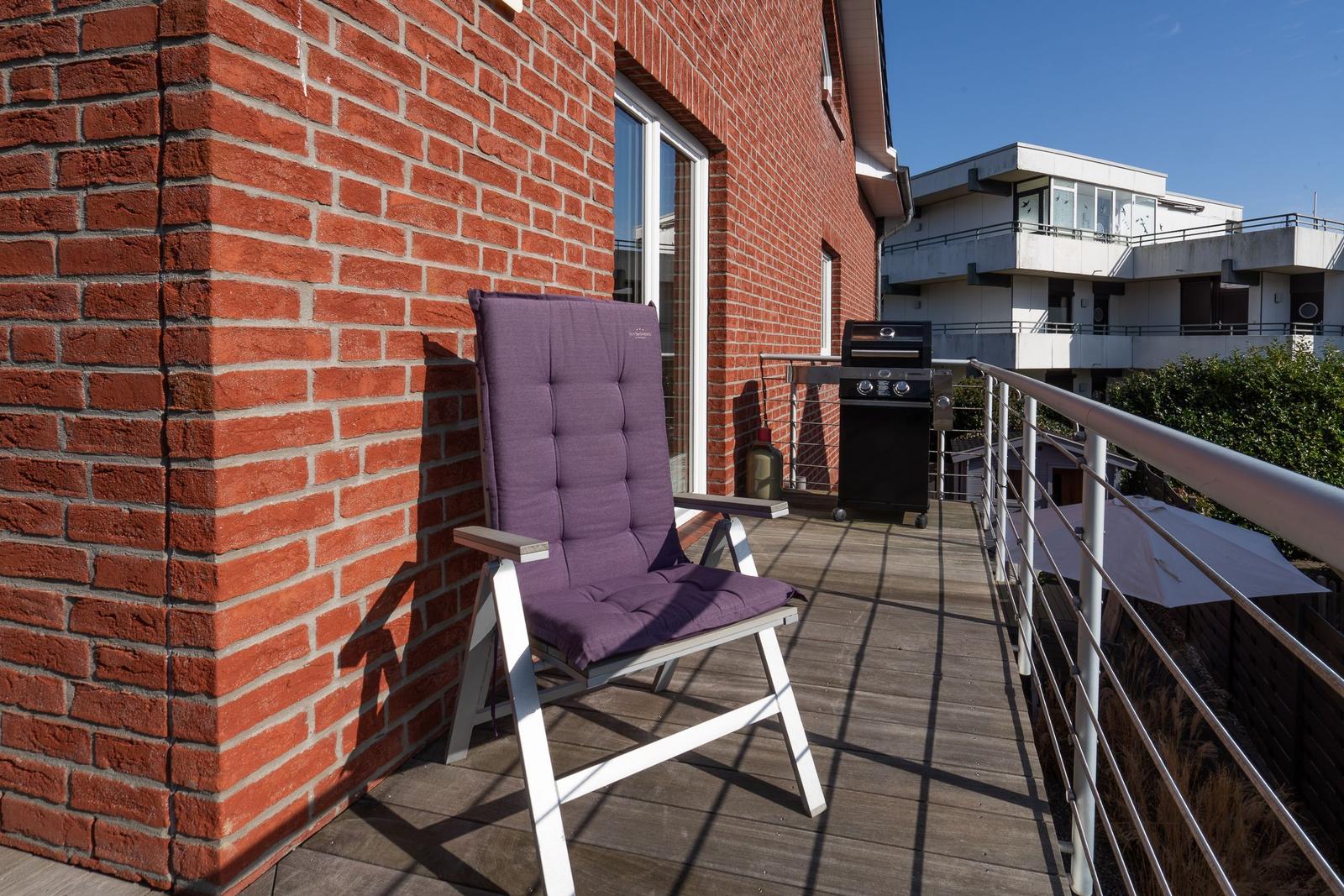 Terrasse mit Stuhl, Grill und rotem Backsteinhaus im Hintergrund.